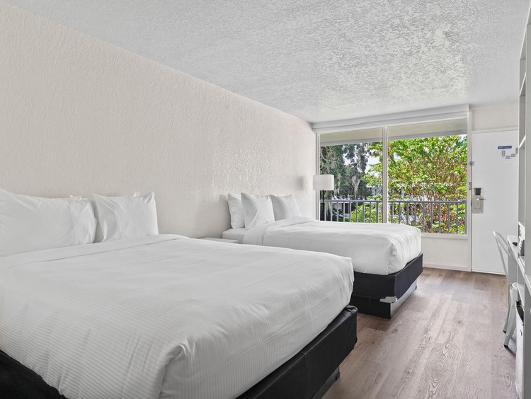 Two double beds with white sheets, view of balcony