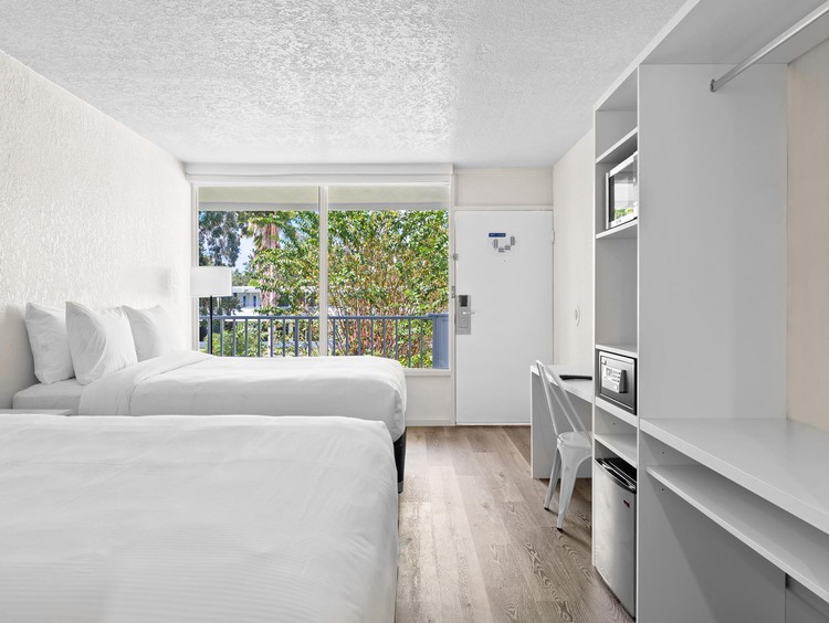 Dos camas dobles con sábanas blancas y vista desde la ventana de los árboles
