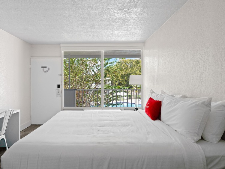 Cama King con sábanas blancas, almohada roja, escritorio y vista al balcón