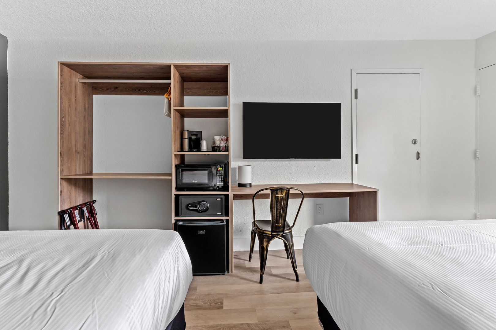 Dos camas dobles, mueble de pared con microondas, caja de seguridad y mininevera junto a TV montada y escritorio