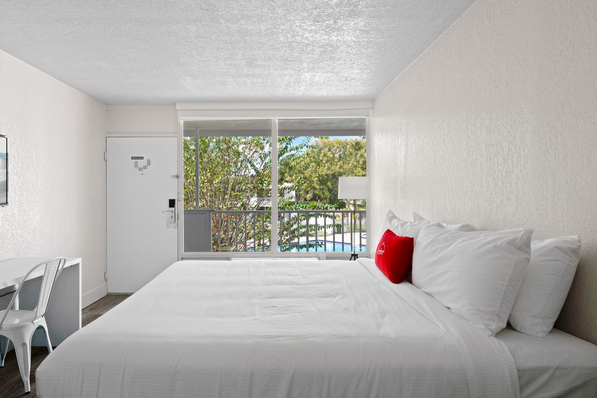 King bed with white sheets, red pillow, and desk with chair