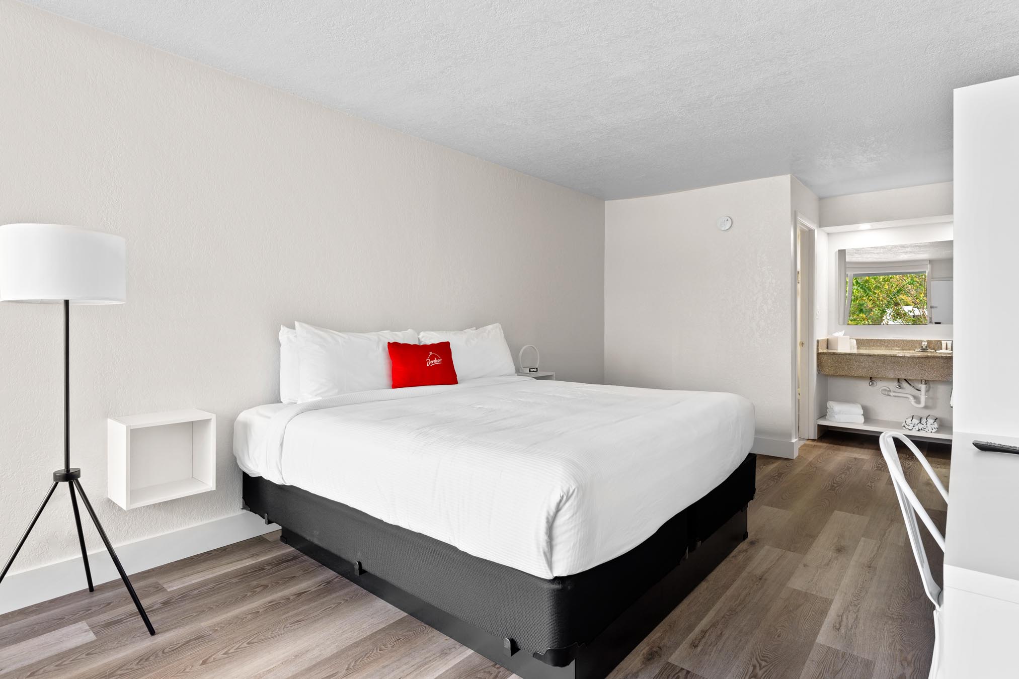 King bed with white sheets, lamp, and desk